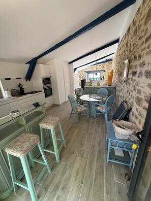 A kitchen with a gas stove, oven, and a dining area with a table and chairs. - QUIET LOFT IN THE COUNTRYSIDE, 7 KM FROM AMENITIES (Saint-Bressou)