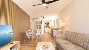Ein modernes Wohnzimmer mit Holzboden, einem gestreiften Sofa, einem Essbereich mit Tisch und Stühlen sowie einer Küche im Hintergrund.