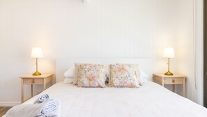 Ein ordentlich bezogenes Bett mit floralen Kissen, zwei Nachttische mit Lampen und ein Nachttisch aus Holz mit einer Lampe.