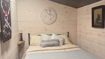 A bedroom with a wooden ceiling, a round wall map, a bed with a patterned blanket, and a framed picture on the wall.