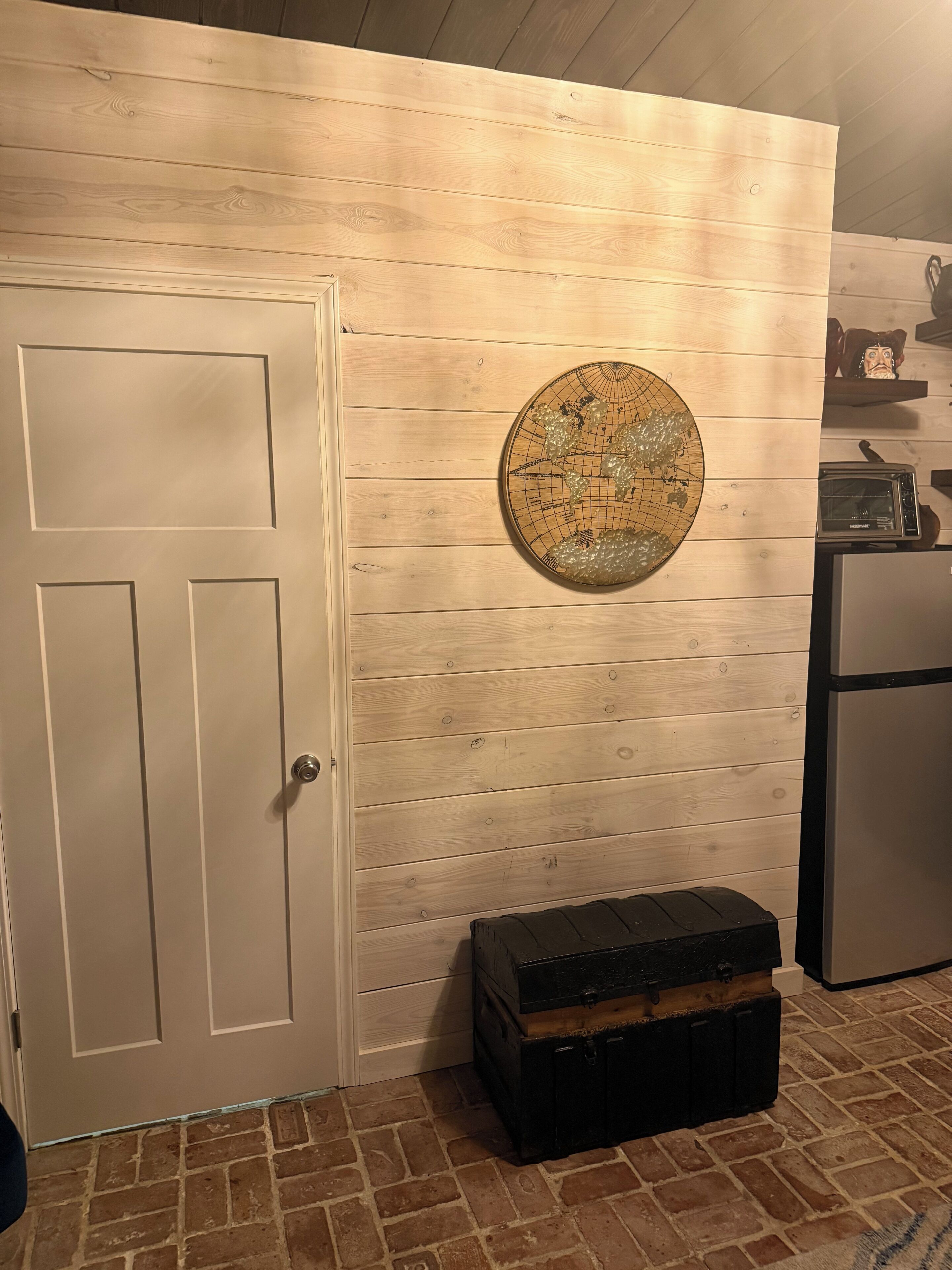 Une cuisine avec un mur en bois, un objet décoratif rond, une commode noire et un réfrigérateur.