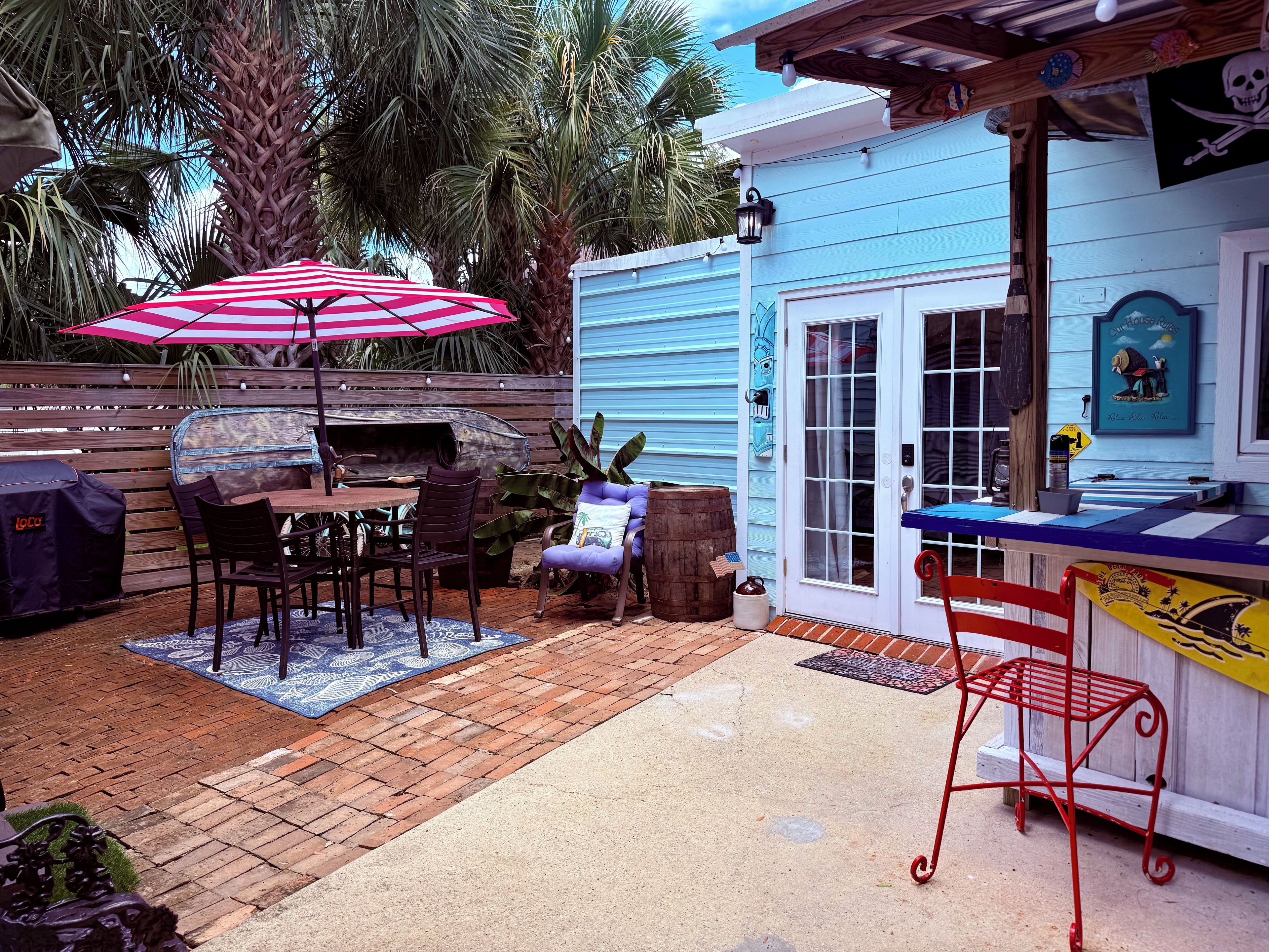 Une terrasse extérieure équipée d’un barbecue, d’une table à manger, de chaises et d’un fauteuil rouge.