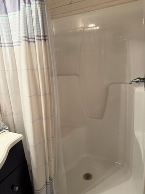 A shower stall with a drain, a white sink, and a black cabinet.