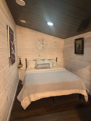 A bedroom with wooden walls, a bed with a quilt, a globe artwork, and a framed picture on the wall.