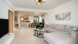 A modern living room with a sofa, a coffee table, and a TV. There is a dining area with a table and chairs. The room has a ceiling light fixture. - Matis Villa Private Pool (Vathi)