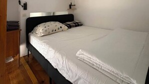 Ein Einzelbett mit weißer Bettwäsche, einem Holz-Kopfteil und einem kleinen Nachttisch mit Lampe.