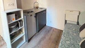 Eine kompakte Küche mit integriertem Geschirrspüler, einer kleinen Spüle und einem weißen Schrank mit Regalen.