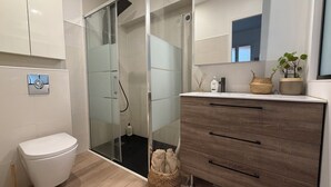 Ein modernes Badezimmer mit Duschkabine aus Glas, einer weißen Toilette, einem Holzwaschtisch mit Schubladen und einem Spiegel über dem Waschtisch.