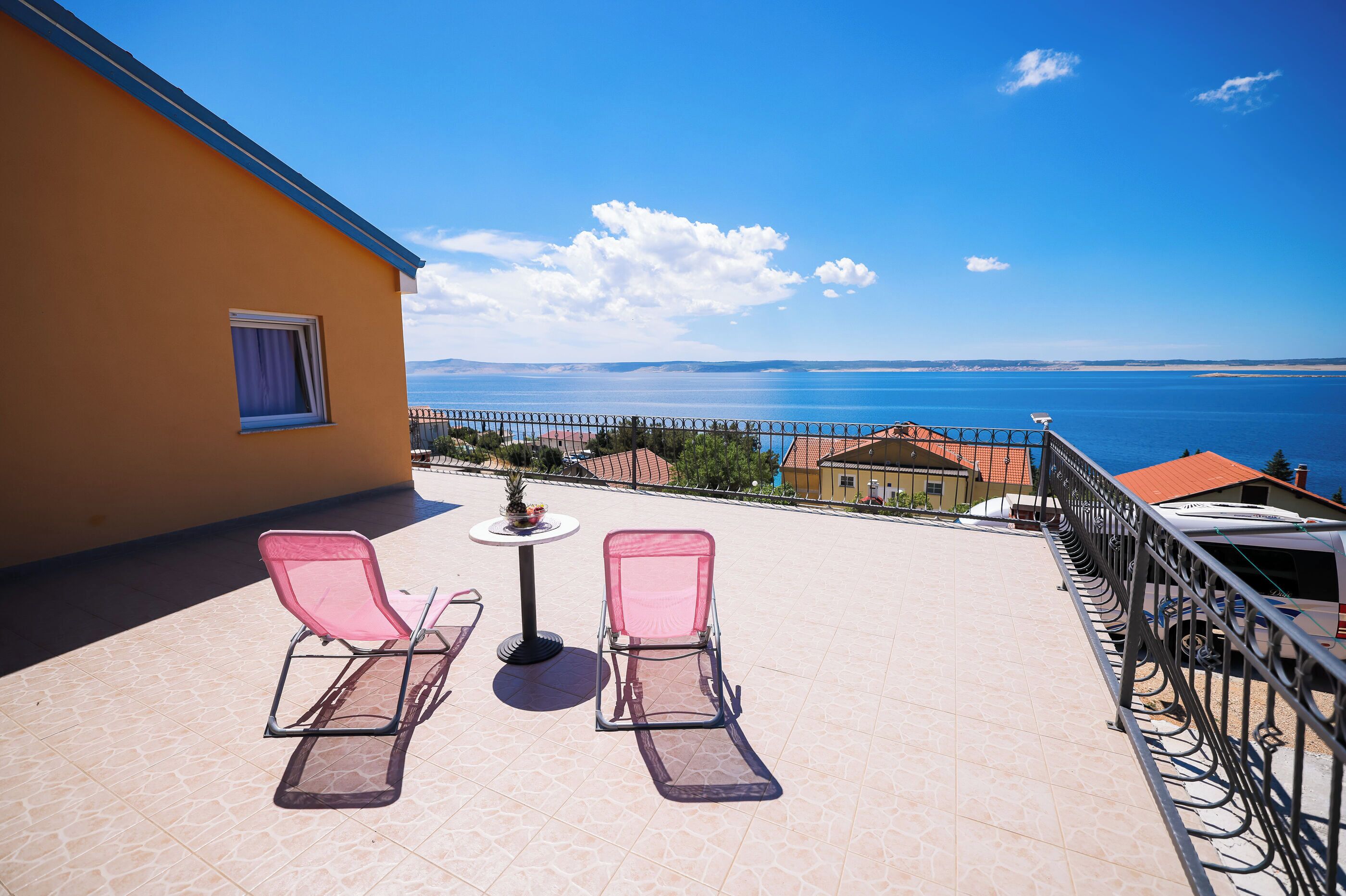 A balcony with two pink sun loungers, a small table, and a view of the sea.