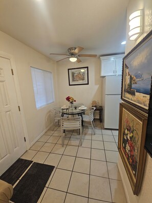 A compact kitchen with a dining area, a ceiling fan, a refrigerator, and a framed painting on the wall.
