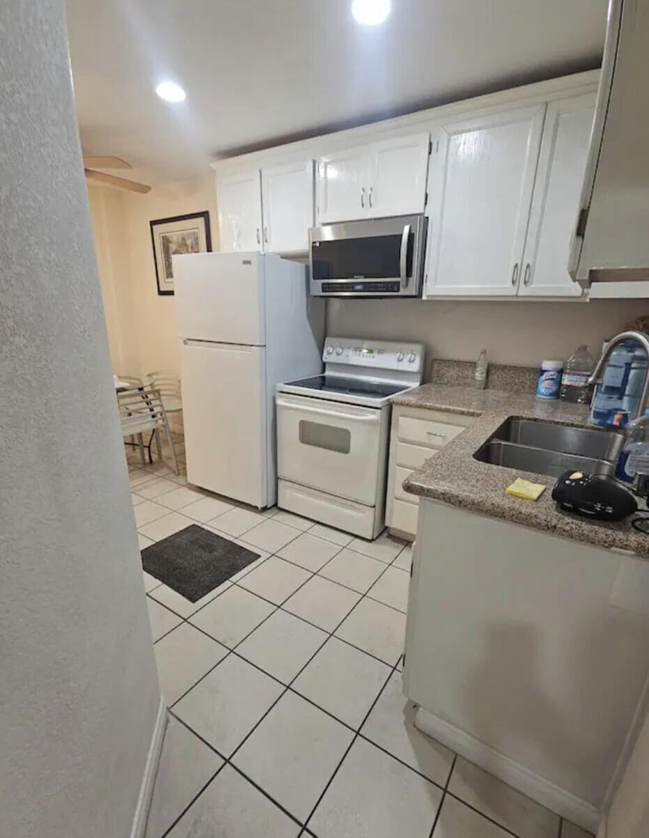 A kitchen with white cabinets, a refrigerator, a microwave, an oven, and a sink.