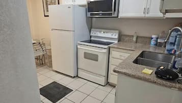 A kitchen with white cabinets, a refrigerator, a microwave, an oven, and a sink.