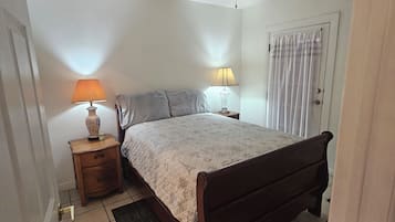 A bedroom with a bed, two bedside lamps, a ceiling fan, a door with a curtain, and a tiled floor.