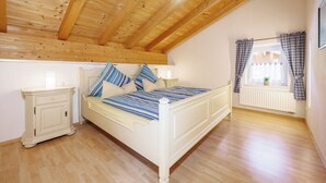 A bedroom with a wooden ceiling, a bed with striped bedding, a nightstand, and a window with curtains. - Hinterseer Vacation Home (Ruhpolding)