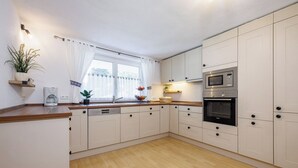 A modern kitchen with white cabinets, a microwave, an oven, a sink, and a window with curtains. - Hinterseer Vacation Home (Ruhpolding)