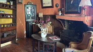 A room with a fireplace, a table with a vase, a chair, and a bookshelf.