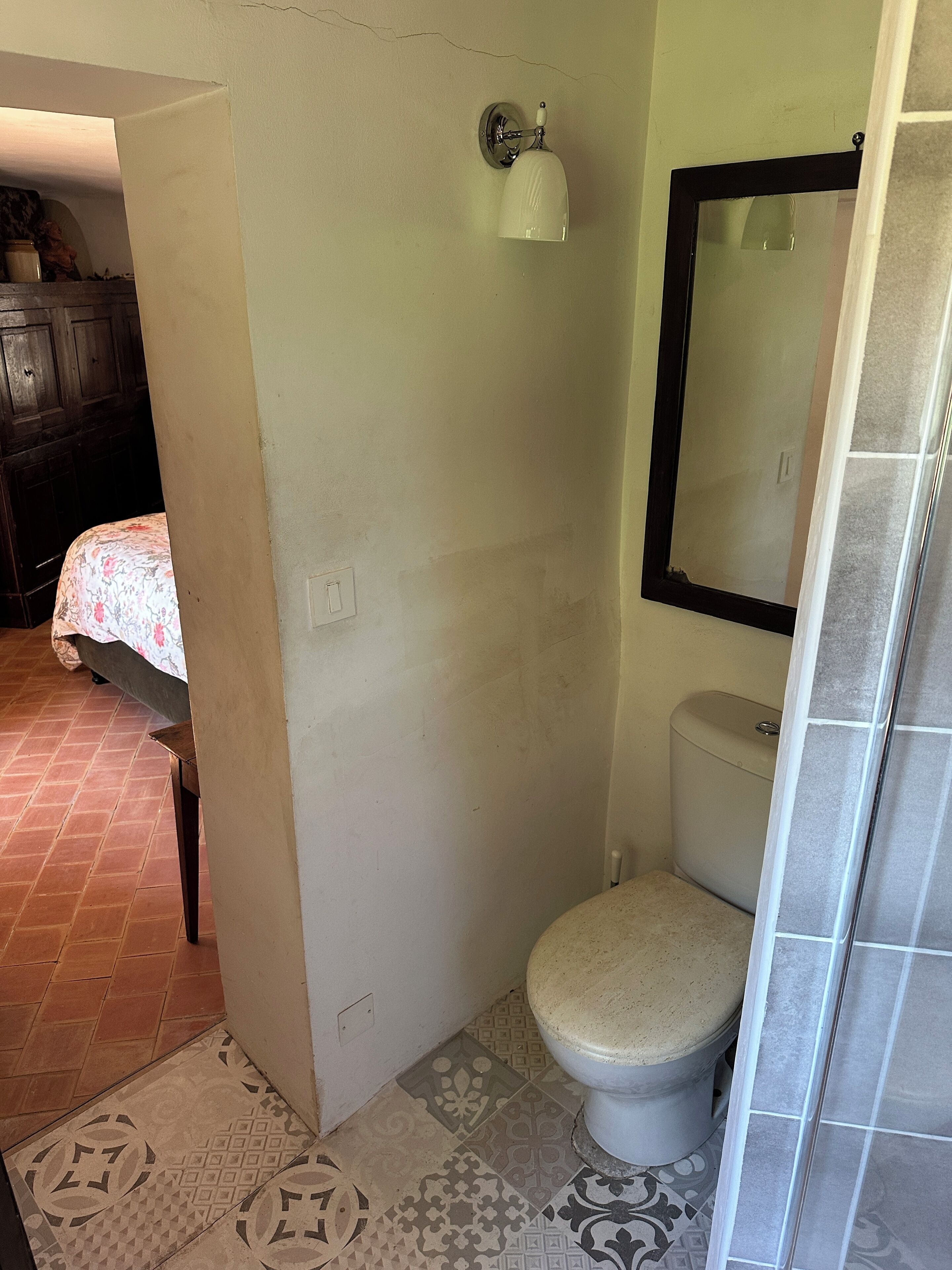 Kylpyhuoneessa on wc, pesuallas ja peili. Viereisessä huoneessa on sängyllä kukkakuviollinen päiväpeite.