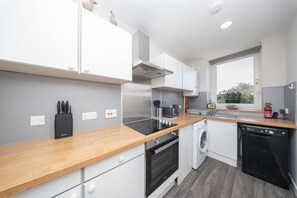 A modern kitchen with a wooden countertop, built-in oven, washing machine, and a window providing a view. - Broughty Ferry 1 Bedroom First Floor Maisonette - Brand New Rental !!!! (Dundee)