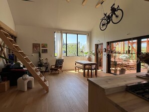 Un amplio salón con una escalera de madera, una mesa de comedor y una bicicleta colgando.