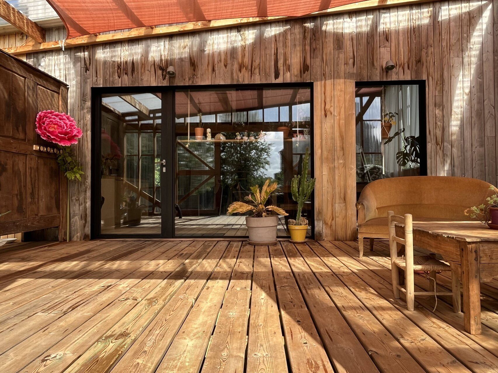 Une terrasse en bois avec une porte-fenêtre en verre, des plantes en pot et une chaise en bois.