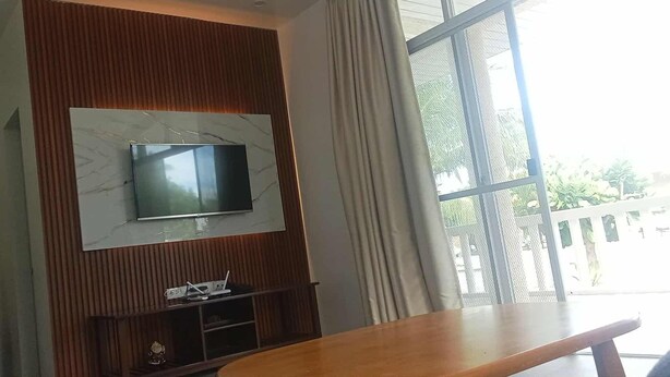 Un salon moderne avec un téléviseur à écran plat fixé sur un mur en marbre, une table en bois et une fenêtre avec des rideaux.