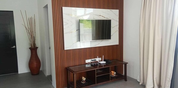A modern room with a large TV mounted on a wall, a wooden console table with a vase and a small figurine, and a door with a dark frame.