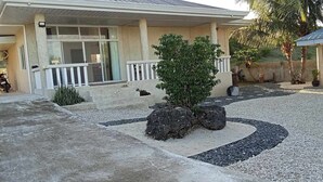 Une maison avec un porche, un petit arbre et une allée gravillonnée.
