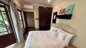 A hotel room with a bed, a wooden nightstand, a door, and a wall-mounted shelf with artwork.