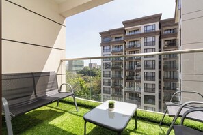A balcony with a sofa, a small table, and chairs, overlooking a residential building. - 108 riverside (Nairobi)