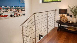 A staircase with a metal railing, a framed beach photograph, a window with a view of greenery, and a small table with a lamp and decorative items. - Contemporary villa with ocean views and a pool, sleeps 10, in Cavalaire-sur-Mer (Cavalaire-sur-Mer)