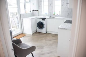Une cuisine moderne dotée d’un lave-linge encastré, de meubles blancs et d’une grande fenêtre.