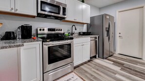 A modern kitchen with white cabinets, stainless steel appliances, a built-in oven, and a refrigerator. - Tranquil Retreat in Spring, The Woodland & Houston (Spring)