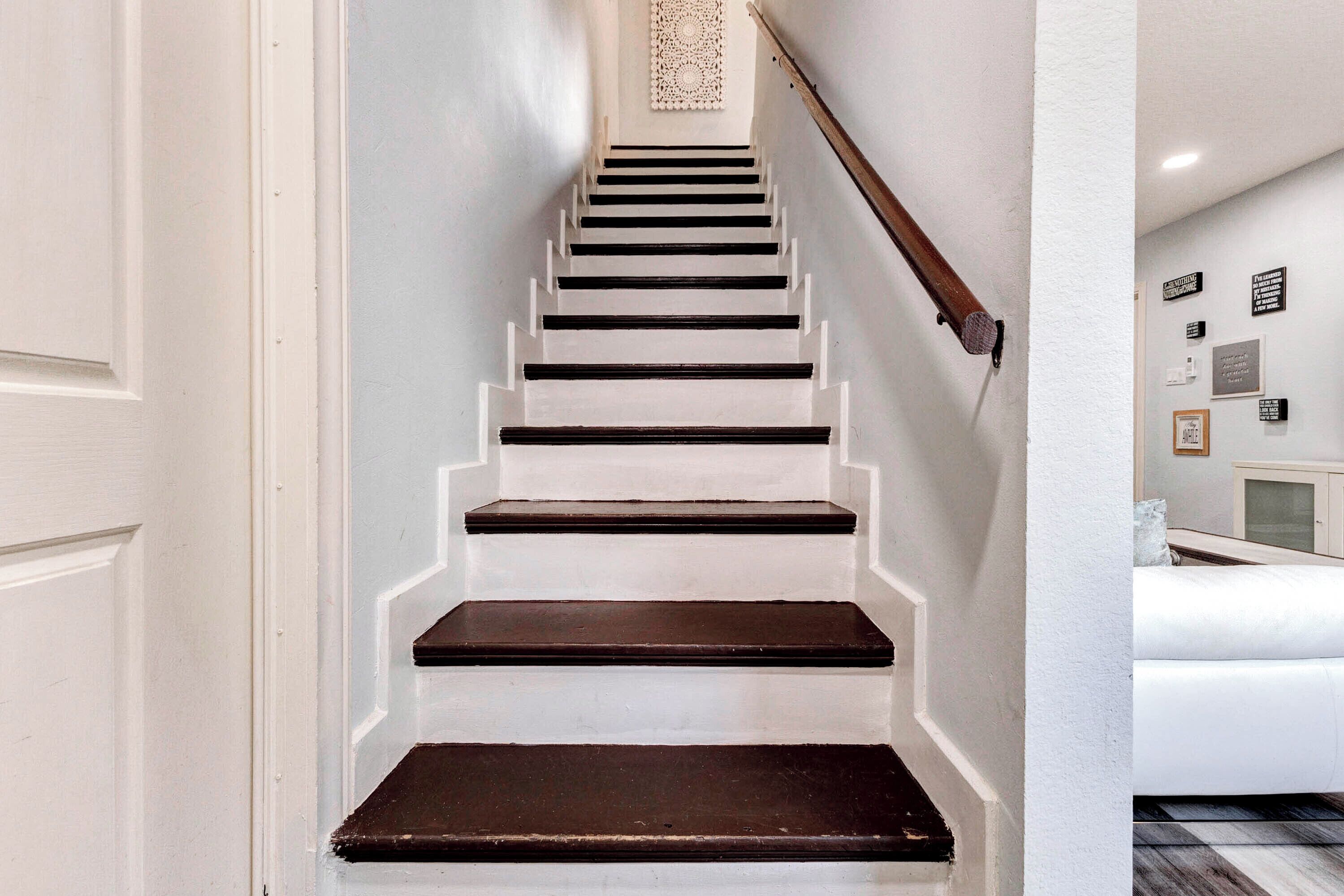 Una escalera con paredes blancas y peldaños oscuros que conduce a un rellano con un tapiz decorativo.