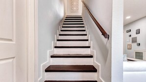 A staircase with white walls and dark steps leading to a landing with a decorative wall hanging. - Tranquil Retreat in Spring, The Woodland & Houston (Spring)