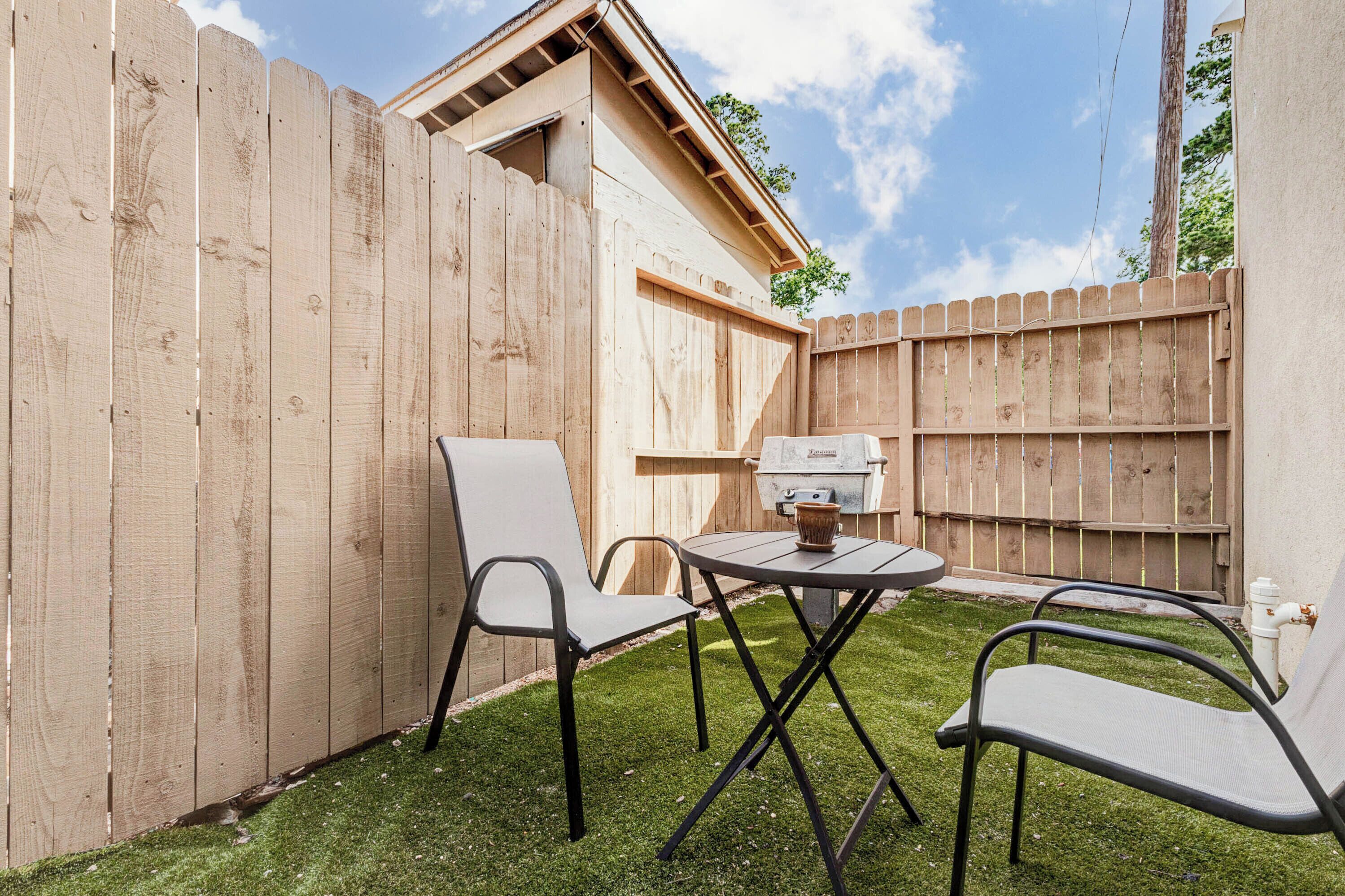 A backyard with a wooden fence, a grill, two chairs, and a table.
