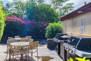 Une terrasse extérieure avec une table ronde et des chaises, un barbecue et, en arrière-plan, une végétation luxuriante.