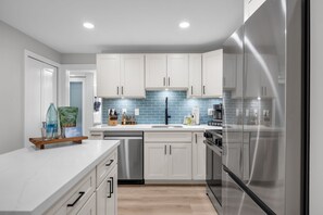 A modern kitchen with white cabinets, a stainless steel refrigerator, and a blue-tiled backsplash. - 2 2 New Designer Beachside Resort Vistas (Kihei)