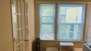 Ein Zimmer mit Holzboden, einer Couch, einer Bank, einem Heizkörper und einem Fenster mit Jalousien.