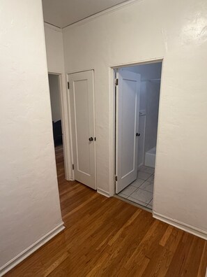 A hallway with wooden flooring, white walls, and two white doors leading to a bathroom. - Rustic 2-bedroom apartment near UC Berkeley for the summer! (Berkeley)