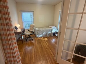 Een slaapkamer met een bed, een bureau met stoel, een raam met zonwering en een deur.