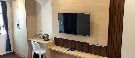 A modern room with a bed, a TV mounted on the wall, a desk with a chair, and a wardrobe.