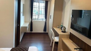 Una habitación de hotel con cama, escritorio con hervidor, televisor y ventana con cortinas.