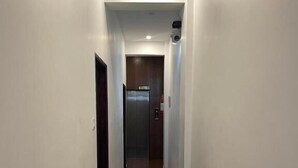 Un pasillo estrecho con piso de madera, paredes blancas y una puerta que da a un ascensor.