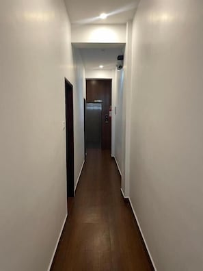 Un pasillo estrecho con piso de madera, paredes blancas y una puerta que da a un ascensor.
