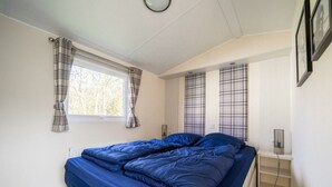 A bedroom with a bed, a window with curtains, a bedside table with a lamp, and a wall-mounted shelf. - Holiday Home in Linden With Terrace (Linden)
