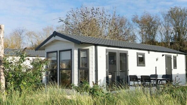 A single-story mobile home with a flat roof, large windows, and a patio area with outdoor seating. - Holiday Home in Linden With Terrace (Linden)