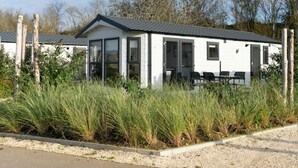 A white mobile home with a tiled roof, large windows, and a patio area with chairs. - Holiday Home in Linden With Terrace (Linden)