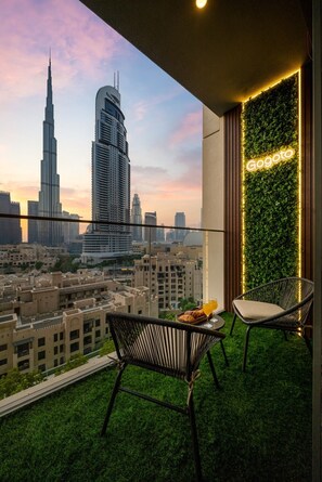 Ein Balkon mit zwei Stühlen, einem Tisch mit Speisen und Getränken und Blick auf die Stadt, darunter ein hohes Gebäude.