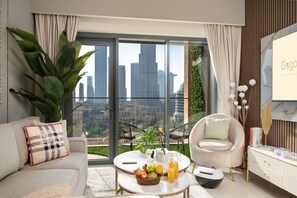 Ein modernes Wohnzimmer mit Stadtblick, einer Couch, einem Sessel, einem Couchtisch mit Früchten und einem Getränk sowie einem dekorativen Spiegel.
