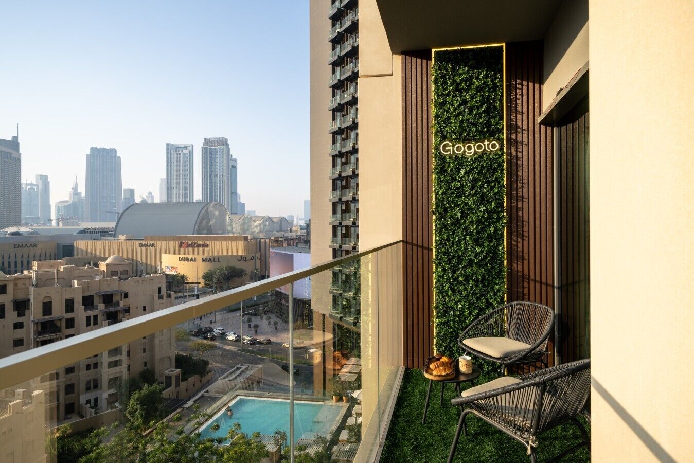 Un immeuble de grande hauteur doté d’un balcon aménagé avec une piscine, une chaise et un jardin vertical portant l’inscription « Gogoto ».